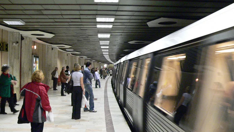 Stație de metrou din București cu afișaj electronic și călători pe peron